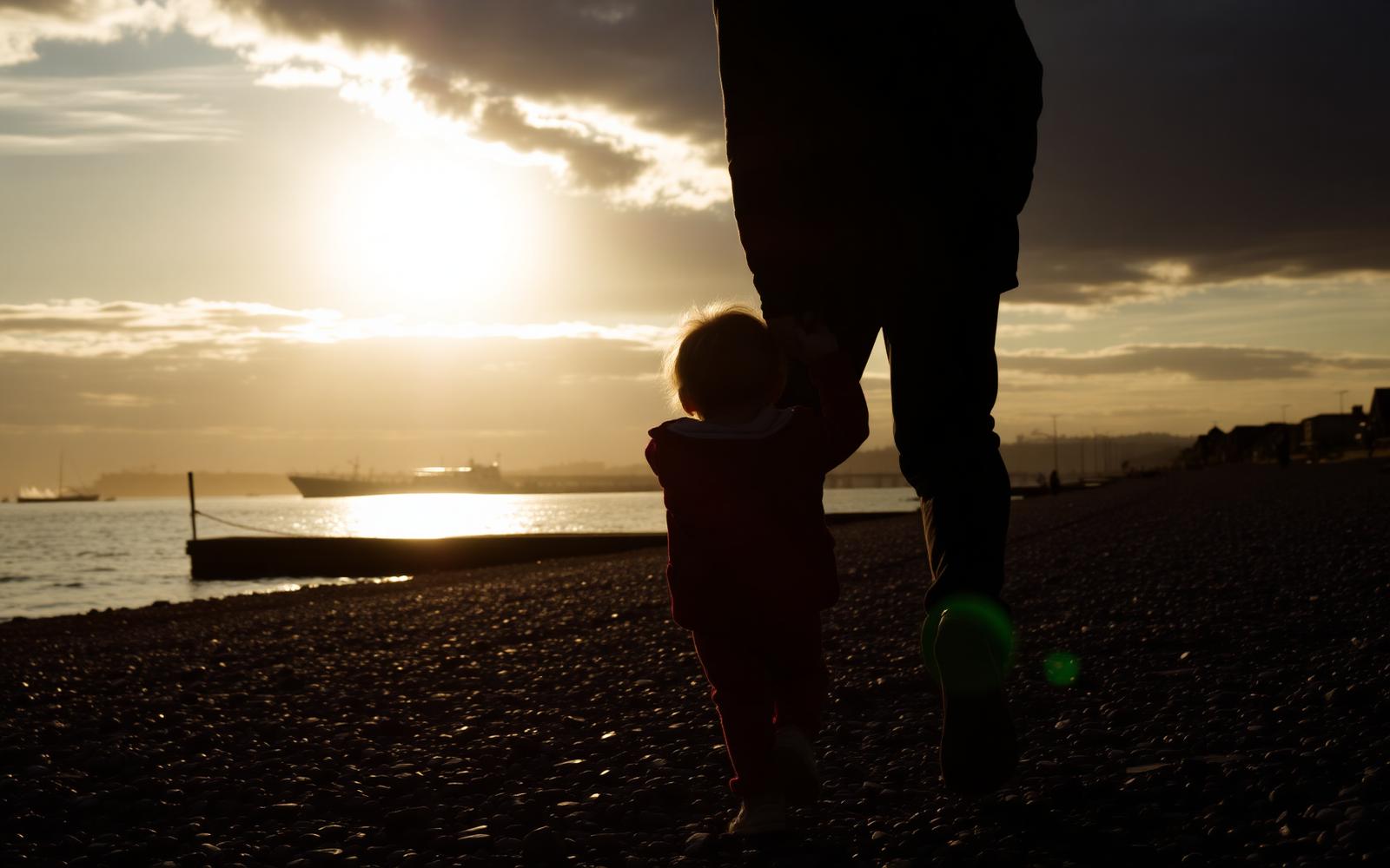 A parent and young child walking hand in hand along the Portsmouth shoreline at sunset